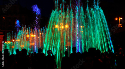 Multi-colored neon lights illuminate the jets of a powerful urban singing fountain in the late evening. photo