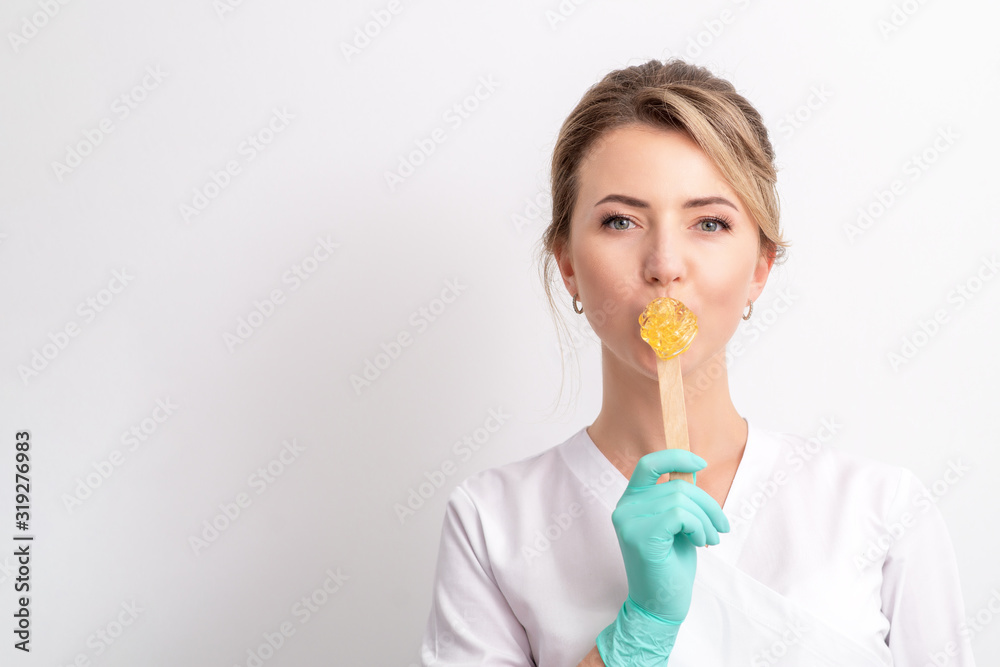 Female cosmetologist holding stick with wax next to lips on white background, copy space. Female cosmetologist holding stick with wax next to lips on white background, copy space.