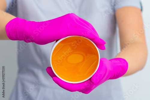 Beautician holding jar with liquid yellow paste for sugaring, close up. © okskukuruza