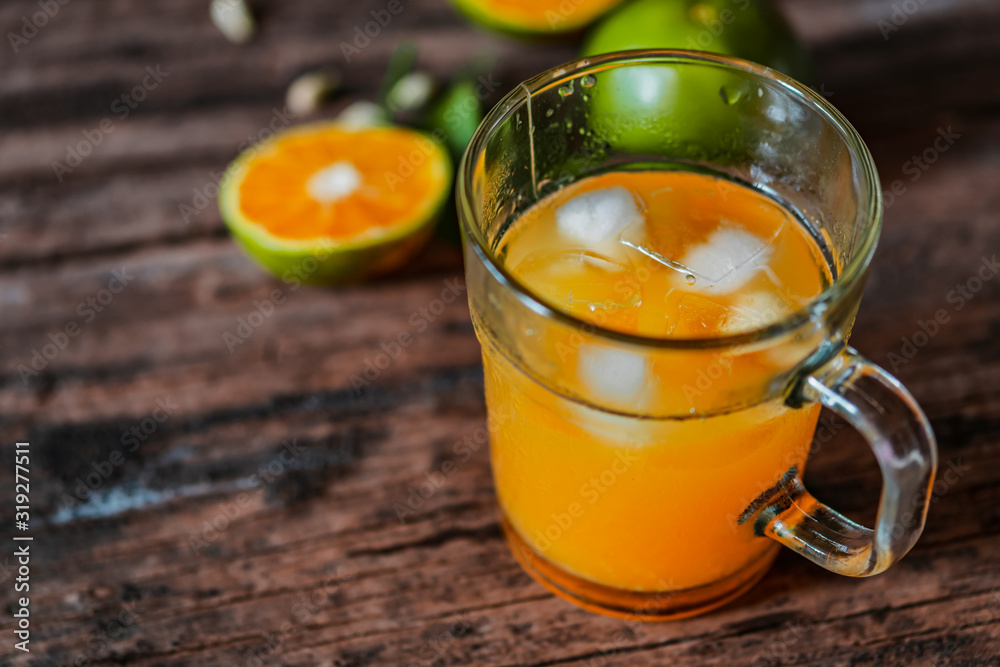 A glass of orange juice on a vintage wooden table, complemented by slices of fresh local oranges and their leaves. In Indonesia this drink is called jus jeruk.