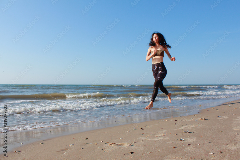 Sporty girl training outside. She is running by seaside. Athletic Fitness Woman Running on the Beach. Female Runner Jogging. Outdoor Workout. Fitness Concept.  Morning workout and sport activity