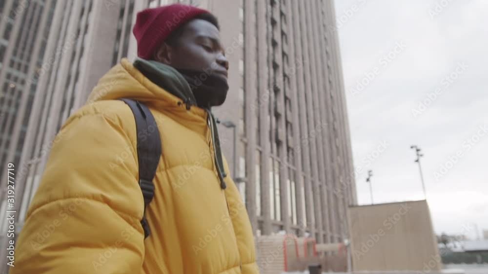 Low angle view of young man wearing warm casual clothes walking in urban area