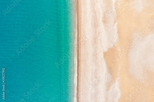 Flying over an empty sandy beach and beautiful emerald ocean waves. Top view landscape scene of waves rolling on an empty tropical beach