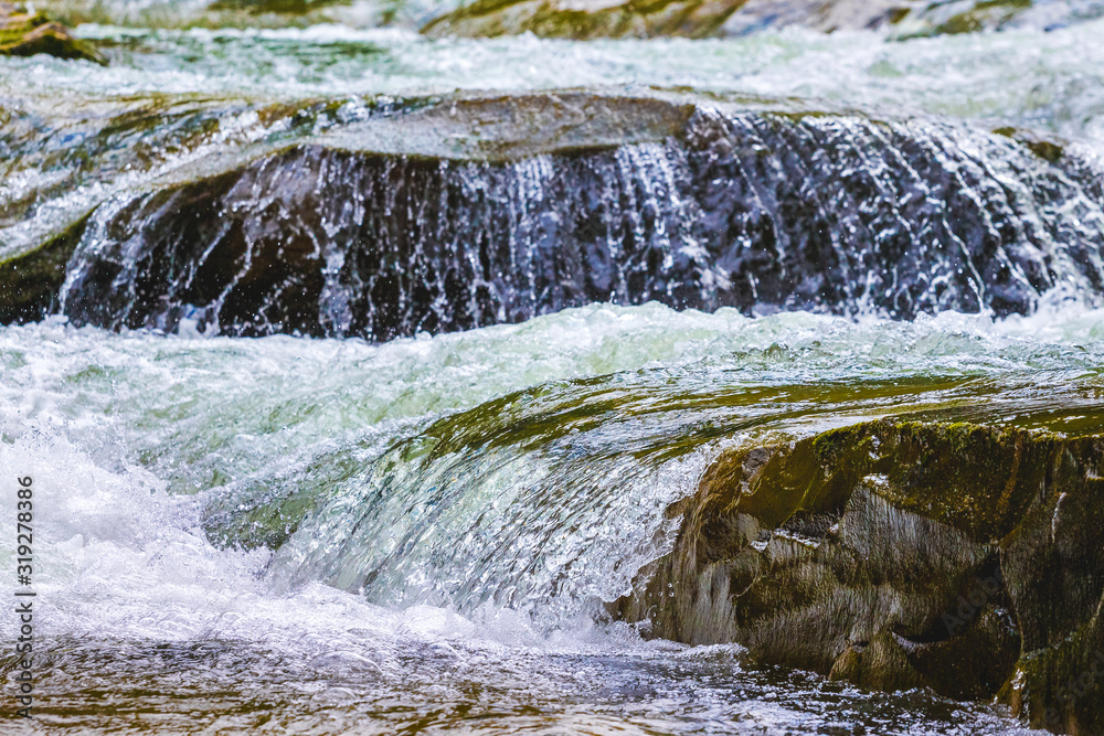 Obraz premium Stormy stream of water in a mountain river with a small waterfall_