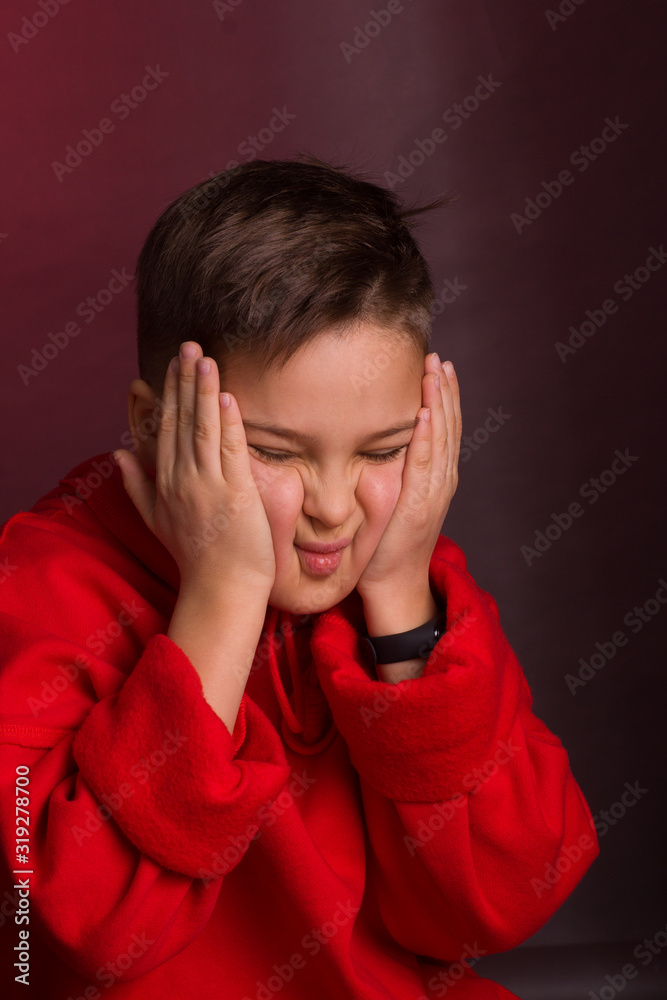 Studio portrait of a dark-haired boy, on a maroon background, in a red hoodie jacket Studio portrait of a dark-haired boy, on a maroon background, in a red hoodie jacket