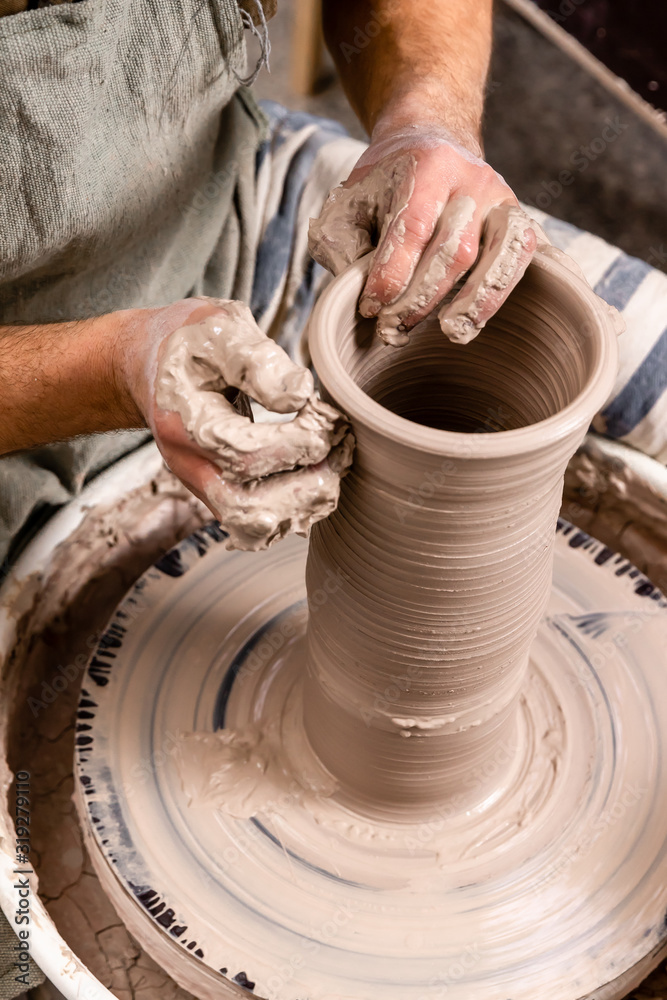 Potter making a jar pot of white clay on the potter's wheel circle in studio, concept of creativity and art, vertical photo