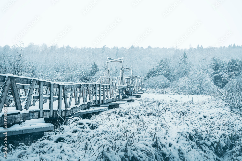 Wooden bridge in the snow covered forest. Side view.