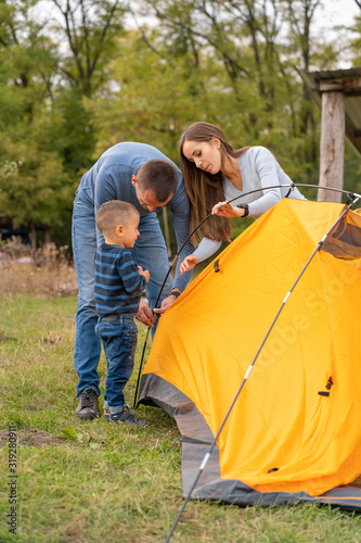 Happy family with little son set up camping tent. Happy childhood  camping trip with parents. A child helps to set up a tent