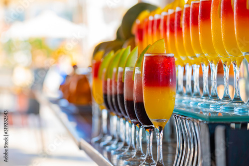 Row of glasses with natural juice on the bar near the pool. Summer luxury tropical restaurant. Elegant cocktails set with fruits.