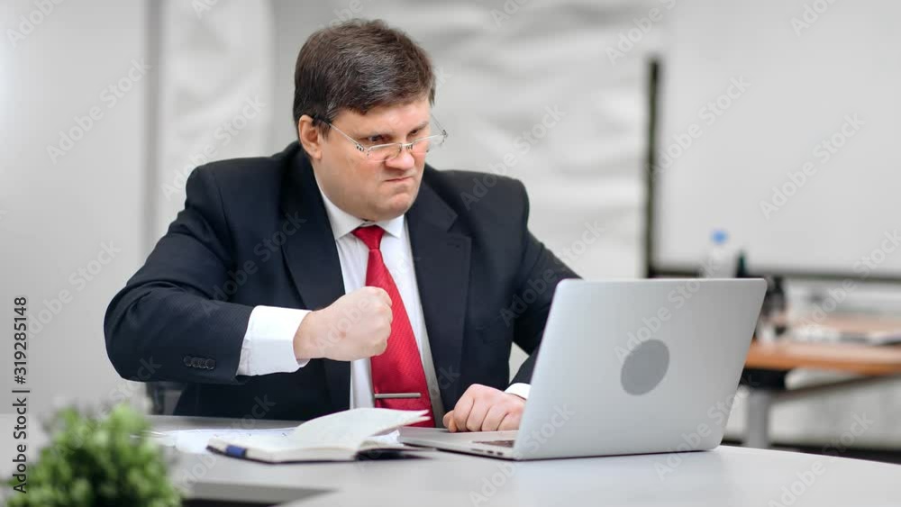 Angry male boss pounding table in fury looking at screen of laptop medium shot on RED camera