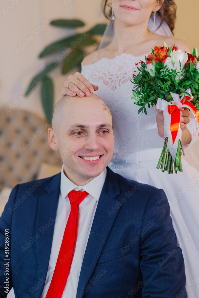 A handsome groom sits on a chair. The bride stands and hugs him. A handsome groom sits on a chair. The bride stands and hugs him.