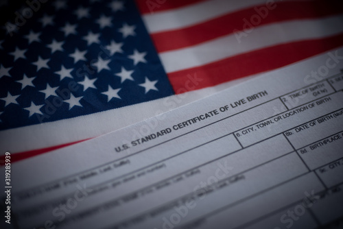 U.S. standard certificate of live birth application form next to flag of USA. Birthright citizenship concept. photo