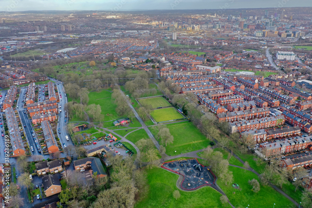Aerial photo of the village of Beeston in Leeds West Yorkshire showing a typical British park along side rows of terrace houses, roads and streets, taken in the winter time on a wet cold day.