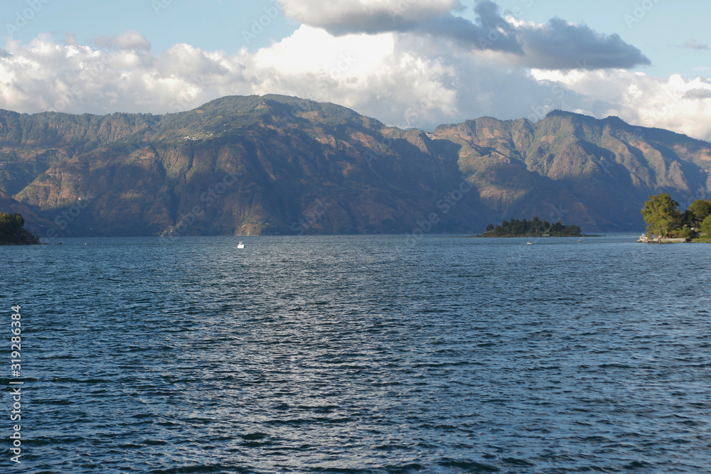 Lake Atitlan surrounded by mountains with pelican flying over the water - cloudy day at the lake in Guatemala