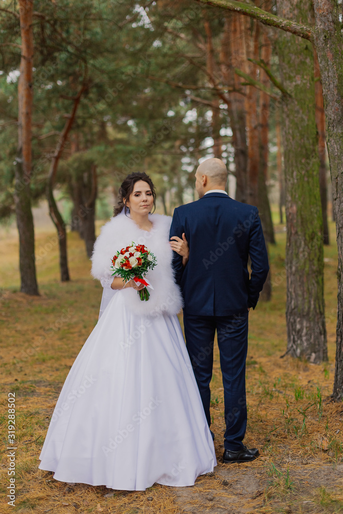 Happy bride and groom are standing in the autumn forest holding hands.