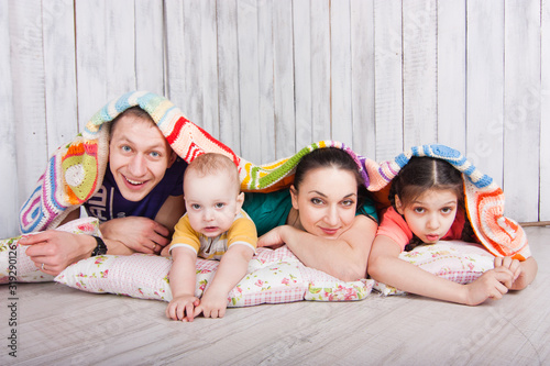 Happy family lie on the floor under colorfull blanket. Indoor photo shot. Empty space for your text