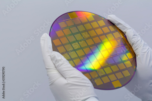 Hands in white gloves holding a silicon wafer on a white background.