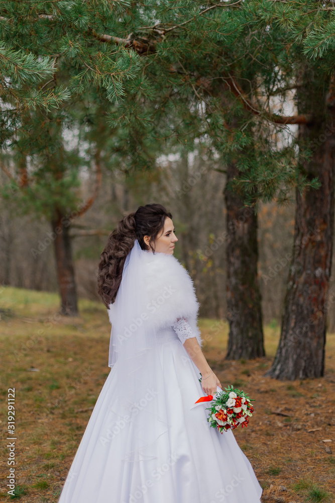 Happy bride in a beautiful wedding dress stands by the pine tree. Happy bride in a beautiful wedding dress stands by the pine tree.