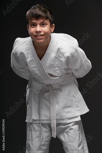 sport concept - a teenager dressed in martial arts clothing poses on a dark gray background, studio shoot