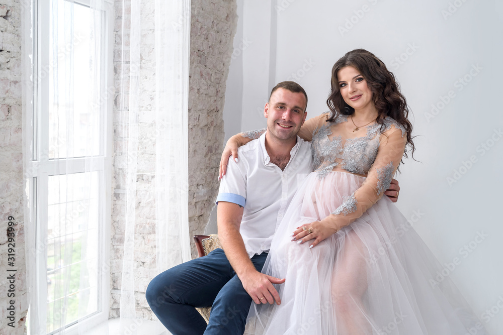 Amazing attractive and pregnant pair posing in studio near window Amazing attractive and pregnant pair posing in studio near window