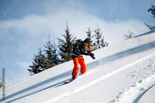 Obraz na plátně Person with dreadlocks and in red pants slides down the mountainside on a snowbo