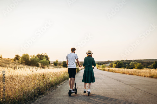 Young couple on vacation having fun driving electric scooter on the road in the countryside. Content technologies. Back view
