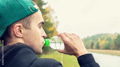 Concept of sports, training and active lifestyle. Young man quenches his thirst after a difficult workout, rear view, 16:9