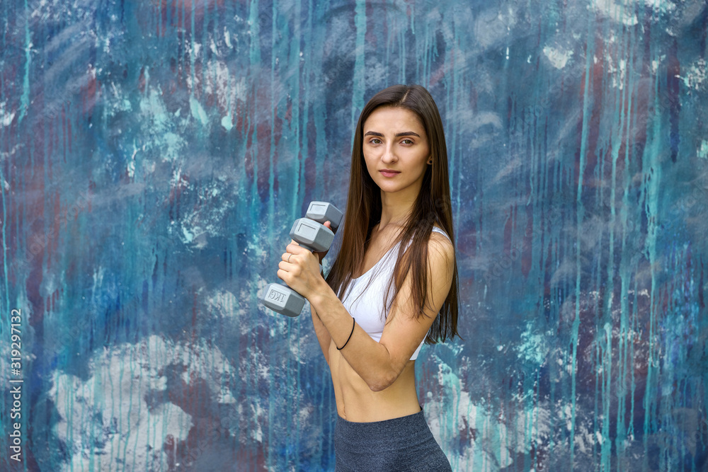 Fototapeta premium Happy young woman with dumbbells making exercises outdoors in front of modern painted wall