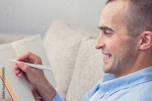 Happy man writing in a notebook, side view, close-up, copy space, toned