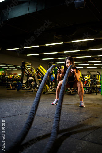 The girl in the gym does an exercise with ropes in her hands.