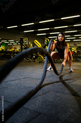 The girl in the gym does an exercise with ropes in her hands.