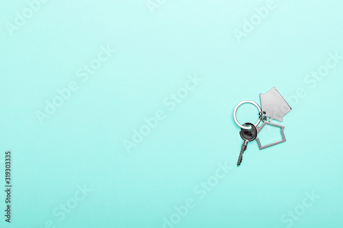 House keys with trinket on color background, top view with copy space. House key on blue background. Minimal flat lay style with place for text.