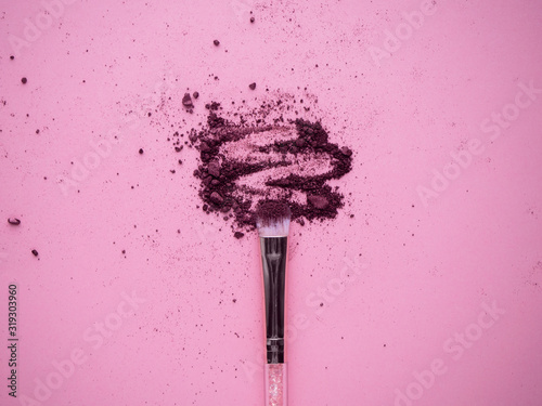 Photo Crushed plum colored shimmer eyeshadows for smokey eyes effect scattered on pink background with nylon makeup brush top view