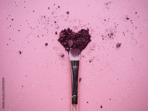 Photo Crushed plum colored shimmer eyeshadows for smokey ice effect scattered in heart form on pink background with nylon makeup brush top view