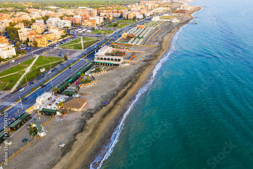 Ostia Lido beach in Italy in warm autumn evening, sandy coast, road near beach and buildings, aerial view.