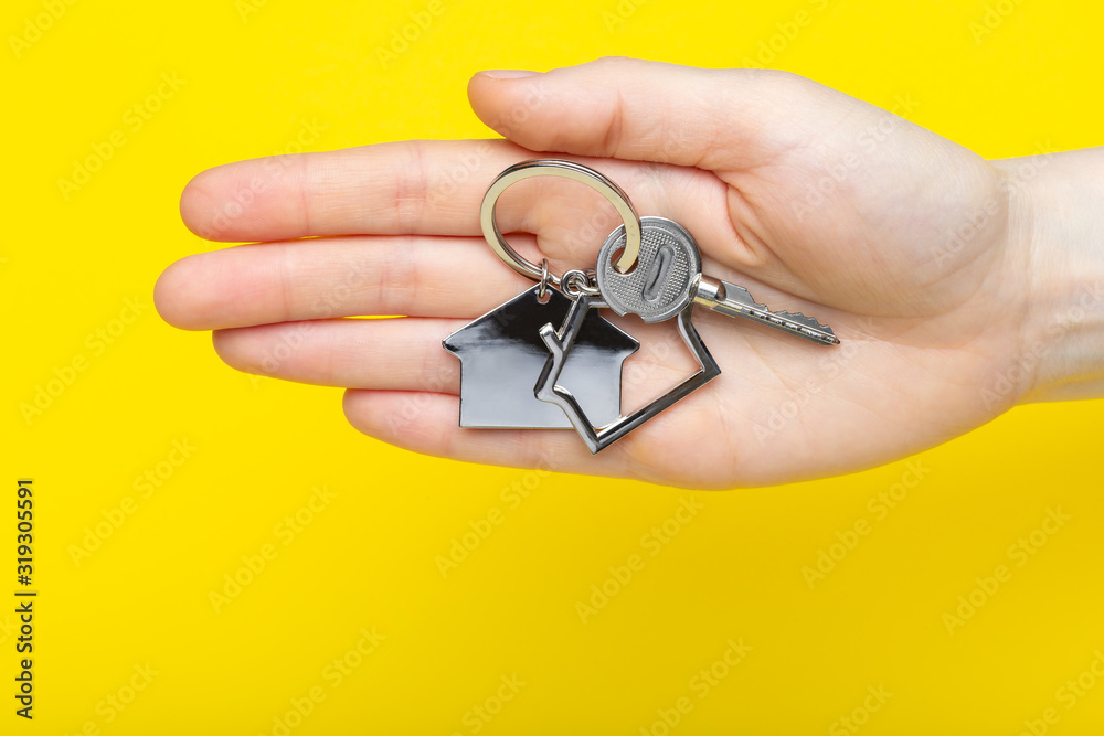 House keys with trinket in female hand on color background, top view with copy space. House key on yellow background. Minimal flat lay style with place for text.