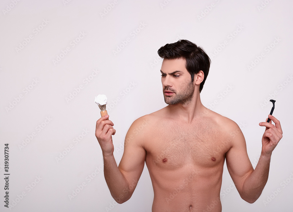 Fototapeta premium A beautiful naked man holds a razor and a shaving anoint.