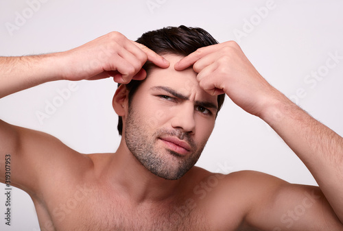 Close-up, a muscular man presses a pimple on his forehead.