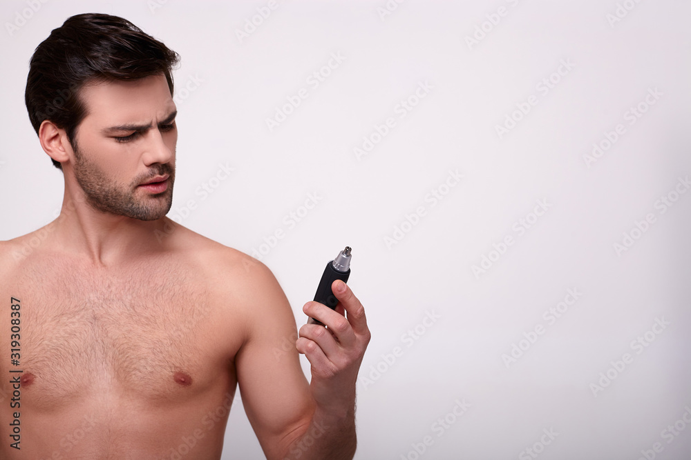 A brooding young guy shirtless with a trimmer in his hand. A brooding young guy shirtless with a trimmer in his hand.