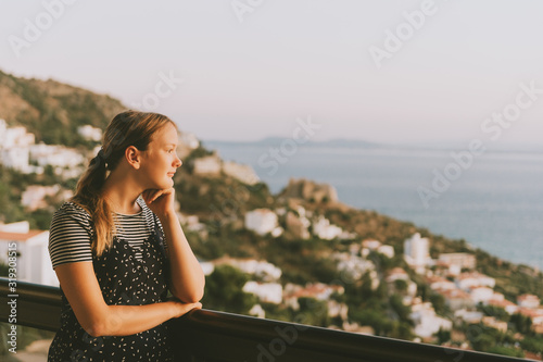 Young girl admiring beautiful landscape from the balcony, summer vacation by the sea, family travel with children