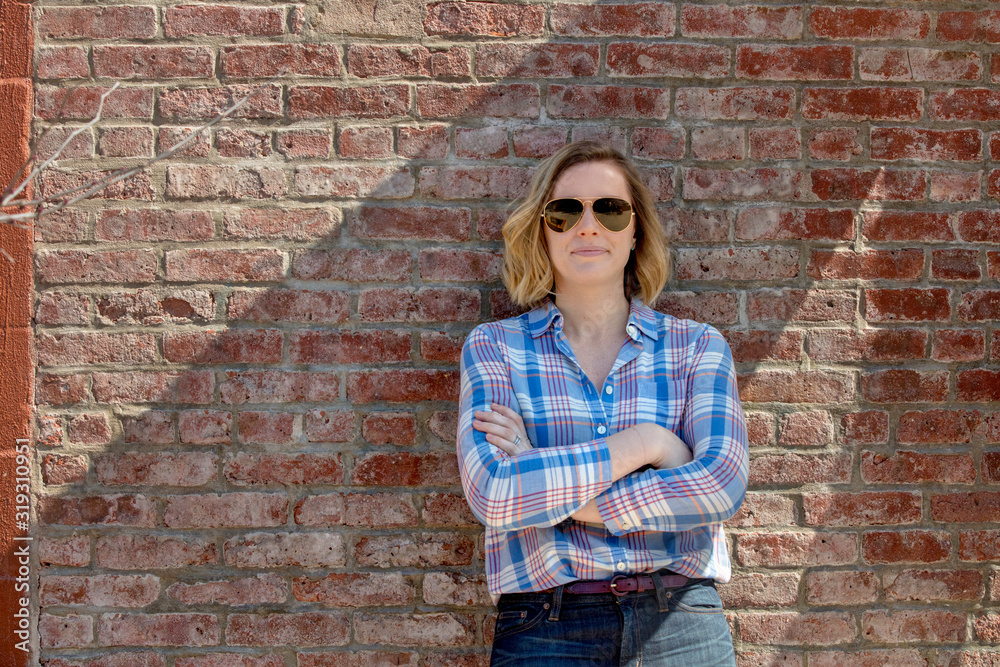 caucasian millennial female business owner on brick wall in plaid shirt with arms crossed caucasian millennial female business owner on brick wall in plaid shirt with arms crossed