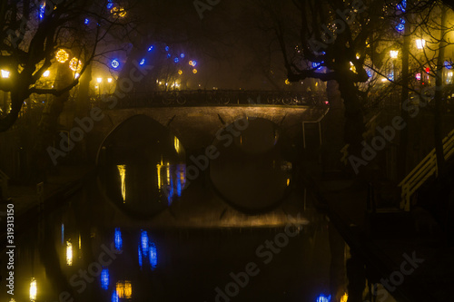  Utrecht  Netherlands  January 21st  2020. Double arc stone bridge across canal in the center of Utrecht. Misty Evening  night view of canal  old dutch houses  bicycles along the canal.