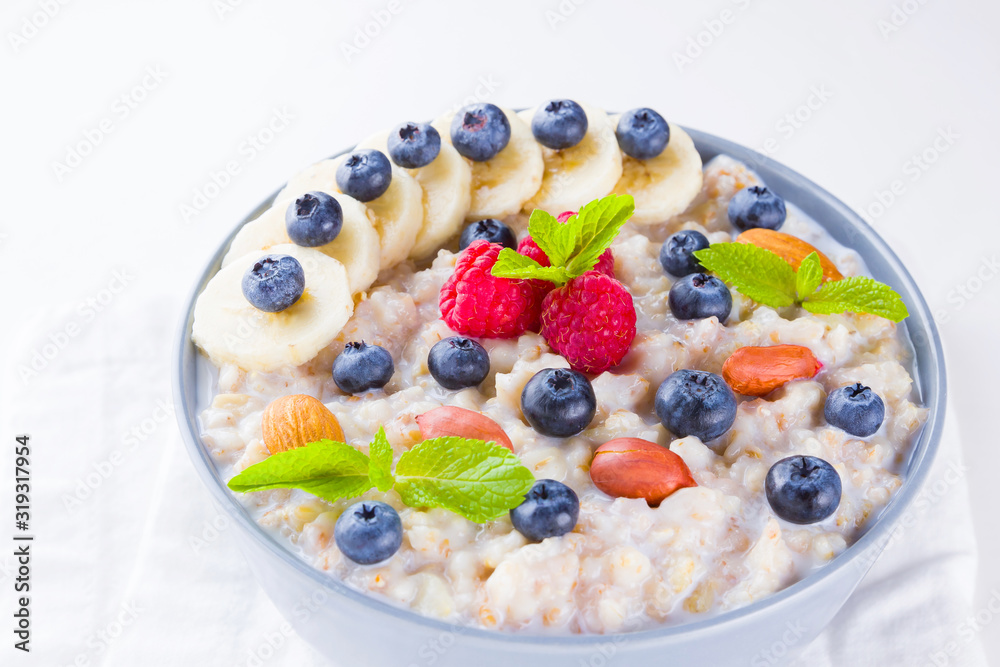 Healthy breakfast. Oatmeal with blueberries, banana and raspberry. Oatmeal with fruits and nuts in a bowl. Cooked oatmeal on white background. Vegetarian food. Copy space Healthy breakfast. Oatmeal with blueberries, banana and raspberry. Oatmeal with fruits and nuts in a bowl. Cooked oatmeal on white background. Vegetarian food. Copy space