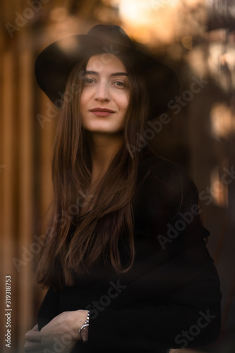 Outdoor photo of brunette lady posing on tree background in autumn day.Fashion street style portrait.Girl wearing dark casual clothes and dark hat .Fashion concept.