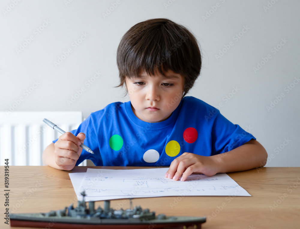 Portrait Cute little schoolboy drawing battleship, Child playing with model ship toy and sketching on paper, Indoors actvitiy concept Portrait Cute little schoolboy drawing battleship, Child playing with model ship toy and sketching on paper, Indoors actvitiy concept