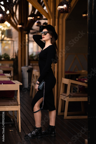 Photo of brunette lady posing on wooden background in cafe.Fashion style portrait. Girl wearing dark casual dress, sunglasses and dark hat .Fashion concept.