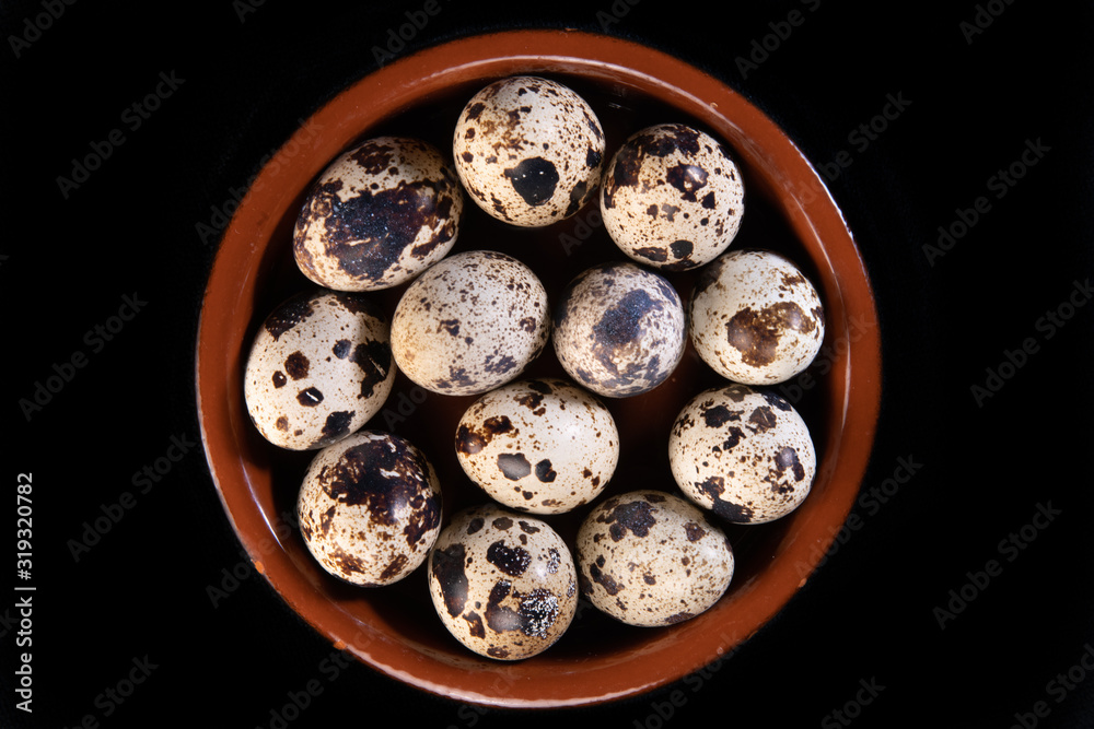 Quail eggs arranged in a small circular earthen dish, on a black background Quail eggs arranged in a small circular earthen dish, on a black background