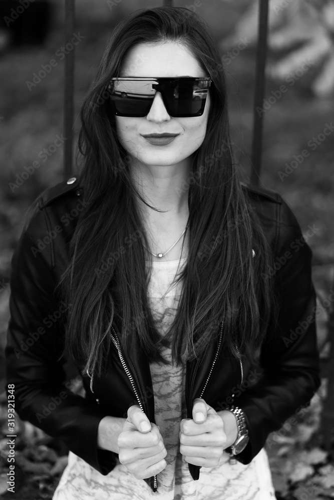 Outdoor fashion portrait of stylish young woman having fun, emotional face , laughing, Urban city street style.Girl wearing white pants,t-shirt, black leather jacket , sunglasses and dark hat Fashion.