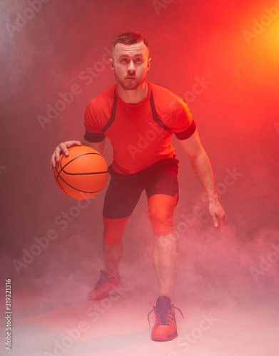 Young athletic man, basketball player preparing for throwing the ball with back lights and smoke on background