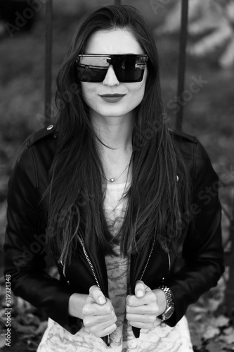 Outdoor fashion portrait of stylish young woman having fun, emotional face , laughing, Urban city street style.Girl wearing white pants,t-shirt, black leather jacket , sunglasses and dark hat Fashion.